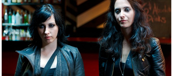 two girls stand staring angry off camera in leather jackets and heavy eyeliner
