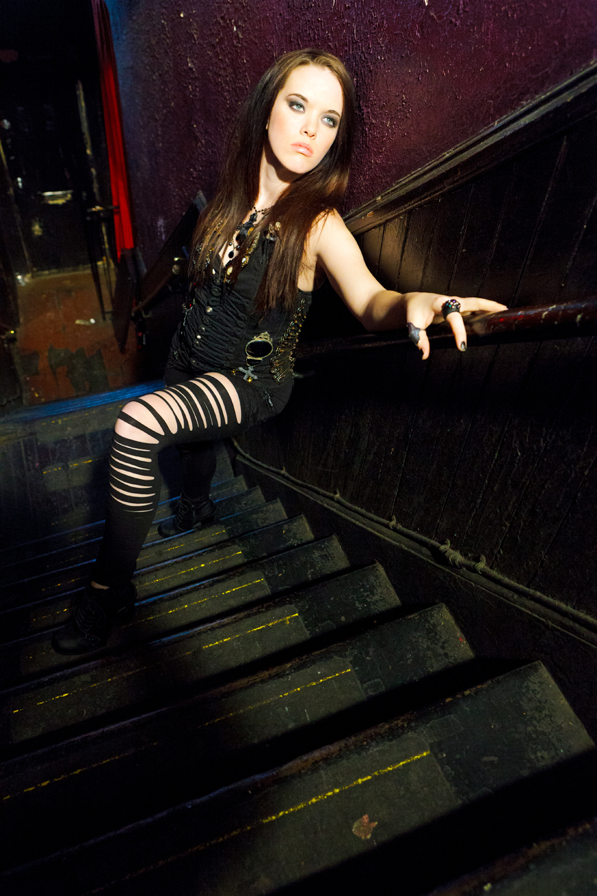 Girl with long black hair and a rockstar outfit walks up a staircase.