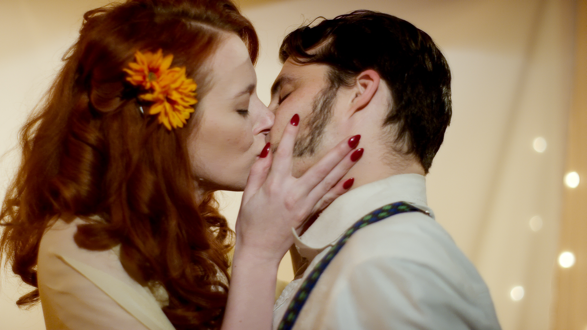Woman with long red hair kisses man with sideburns in a yellow tented room.