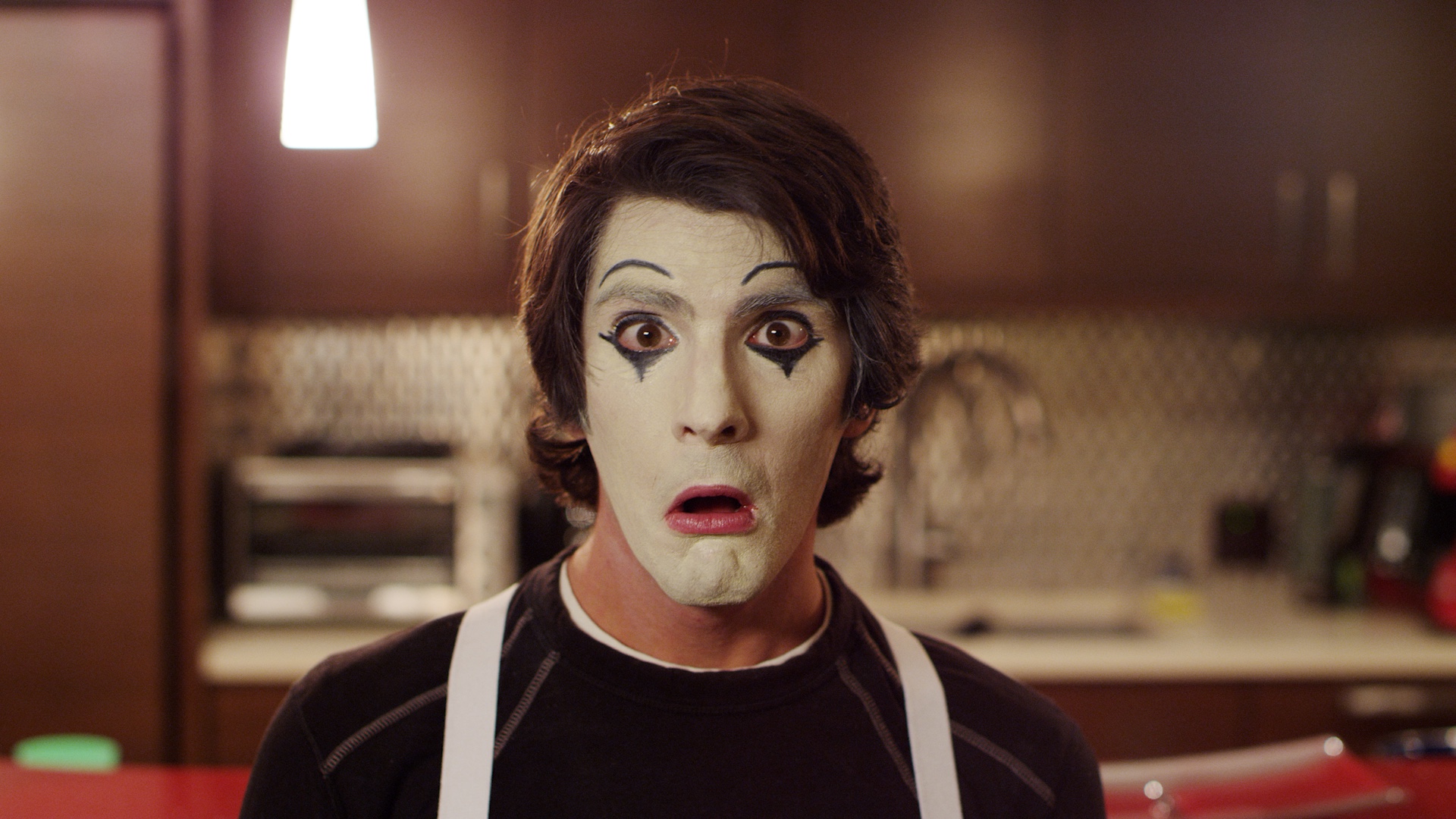 Man with mime makeup on making a shocked expression to camera.