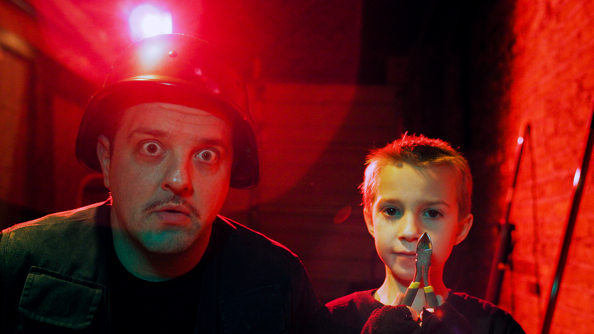 Father and son talking in a red lit room with bomb squad outfit.
