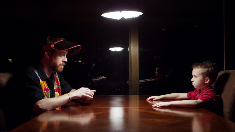 Father and son play Blackjack at a table with a single ceiling light.