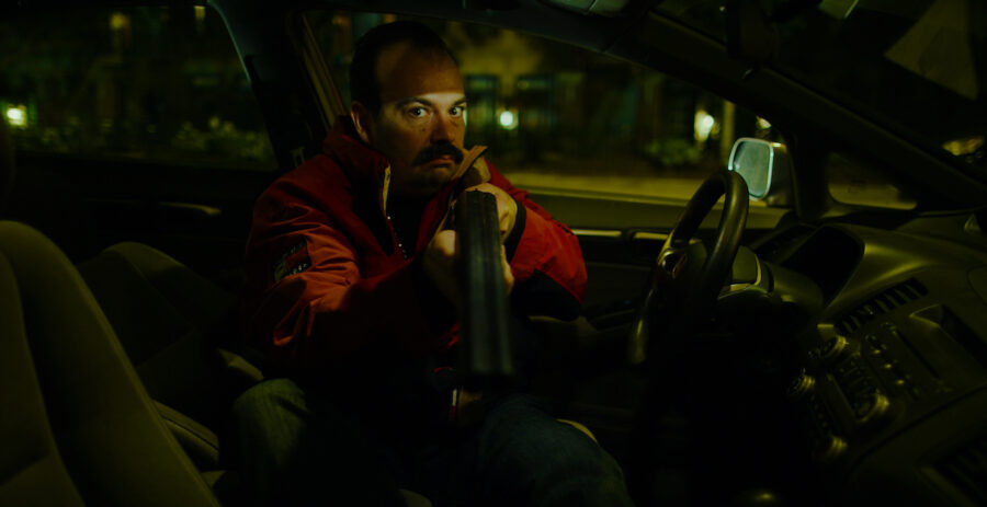 man in car at night points a shotgun out window in the short film 'the Handoff'