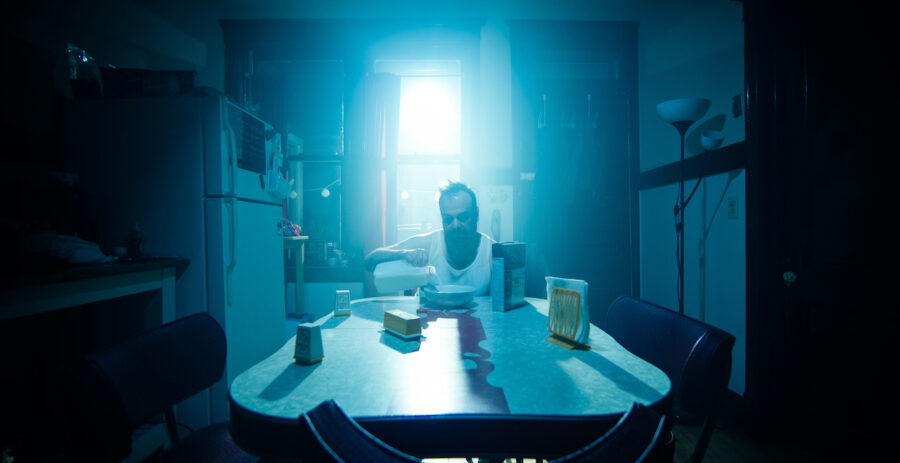 man in blue light sits in kitchen pouring milk in the short film 'the Handoff'