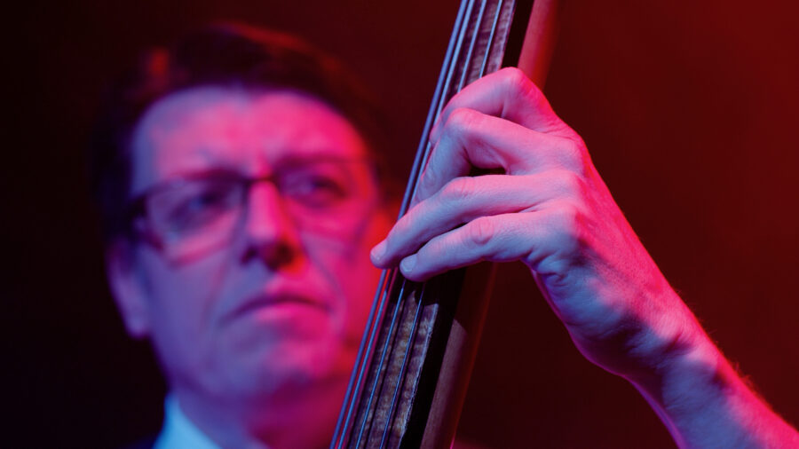 Man with glasses plays guitar onstage with red and blue light.