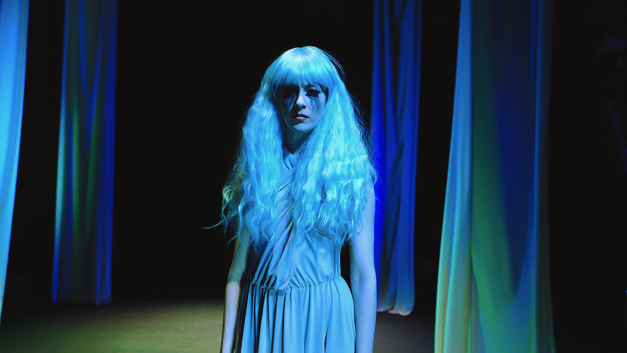 Woman with long hair looks sad in blue light and clown makeup.