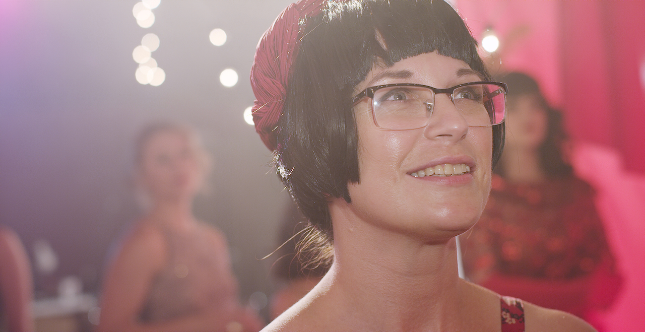 Woman with glasses and red hat looks right in a red tented room with string ball lights.