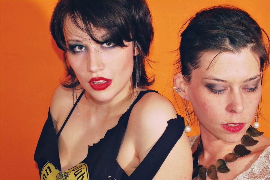 Models in front of a orange wall with red lipstick and white lace.