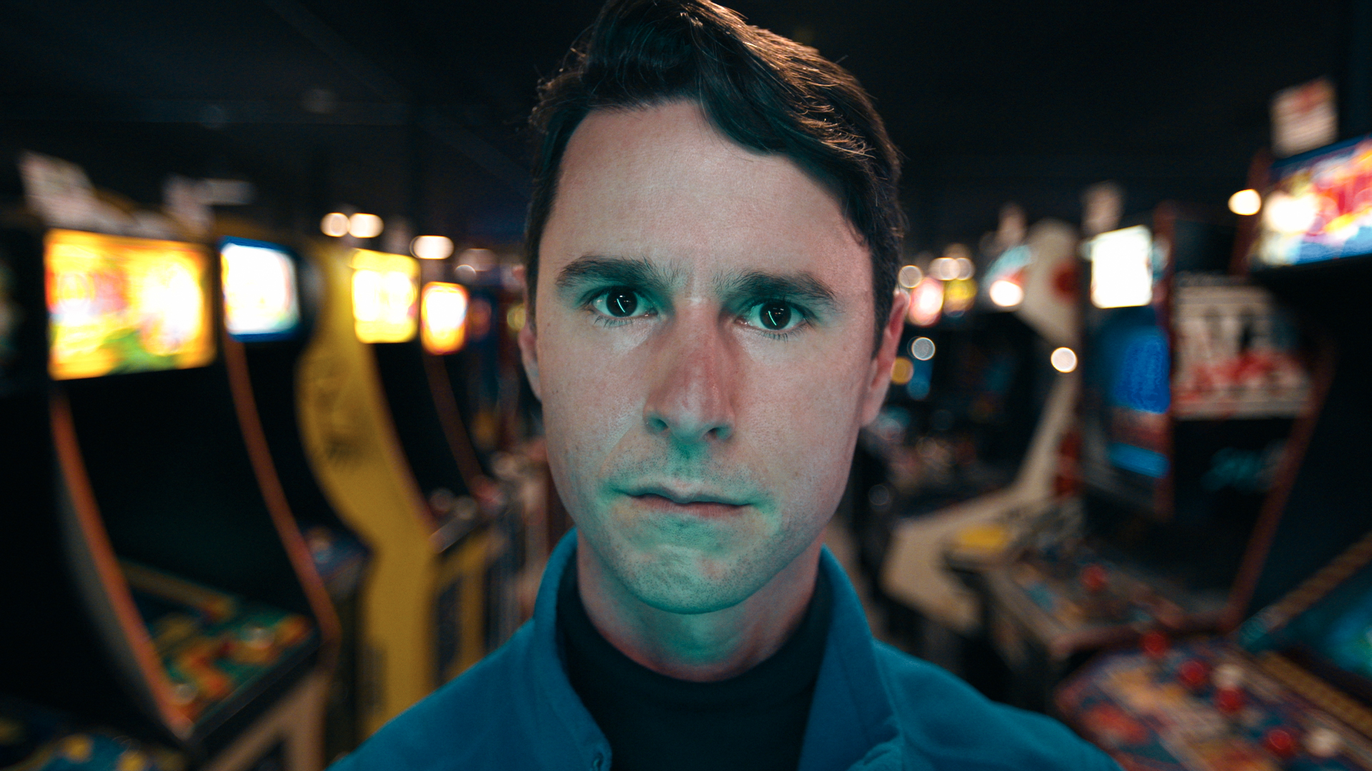 man stares into camera surrounded by arcade games