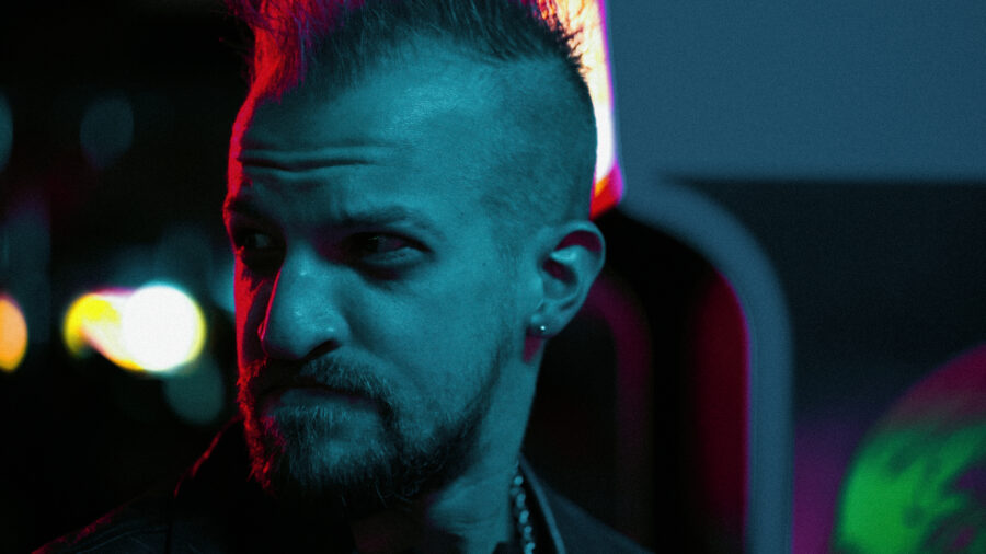 man in blue light turns to the side with a red glow and mohawk