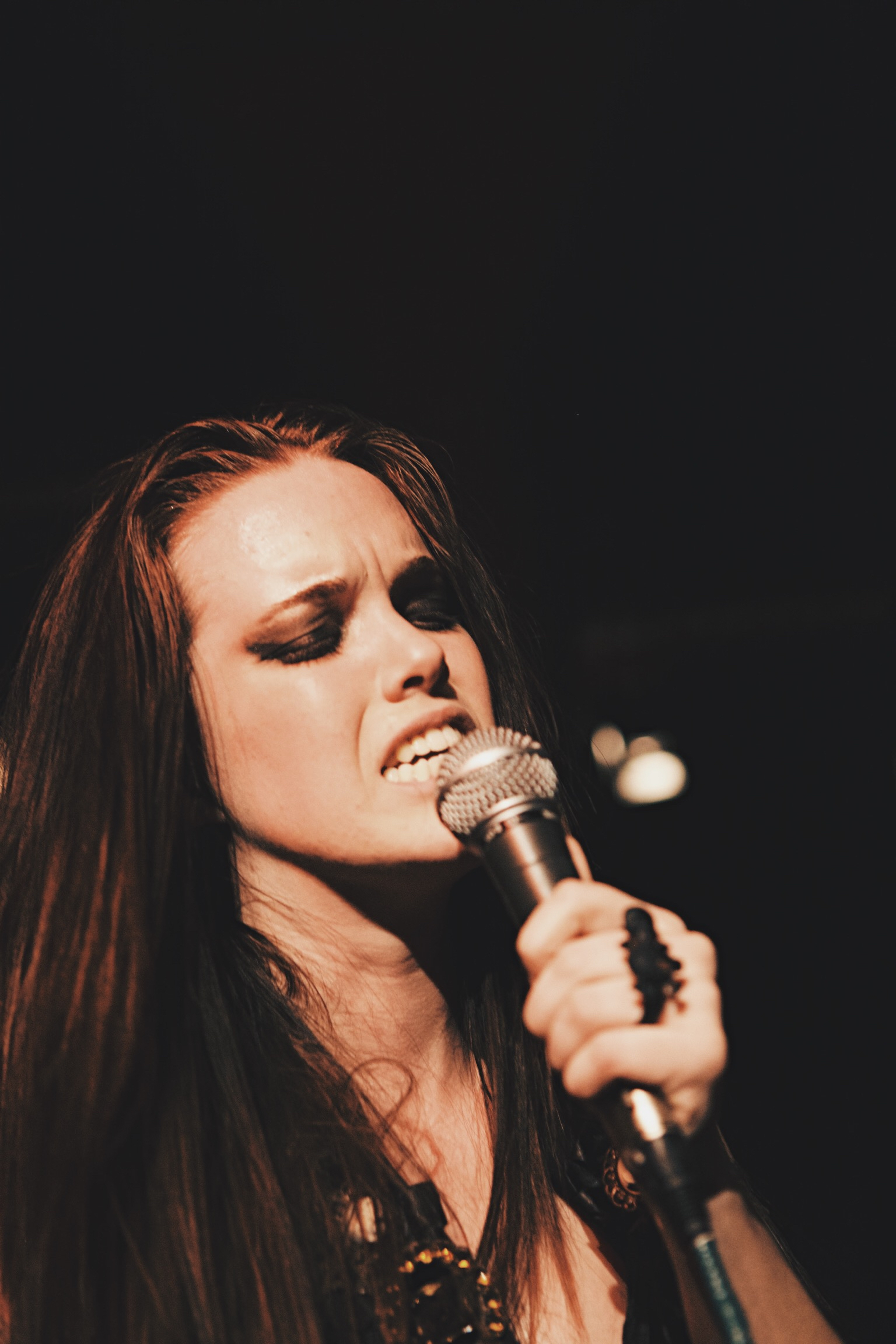 Girl with heavy eye makeup and long hair singing into a microphone.