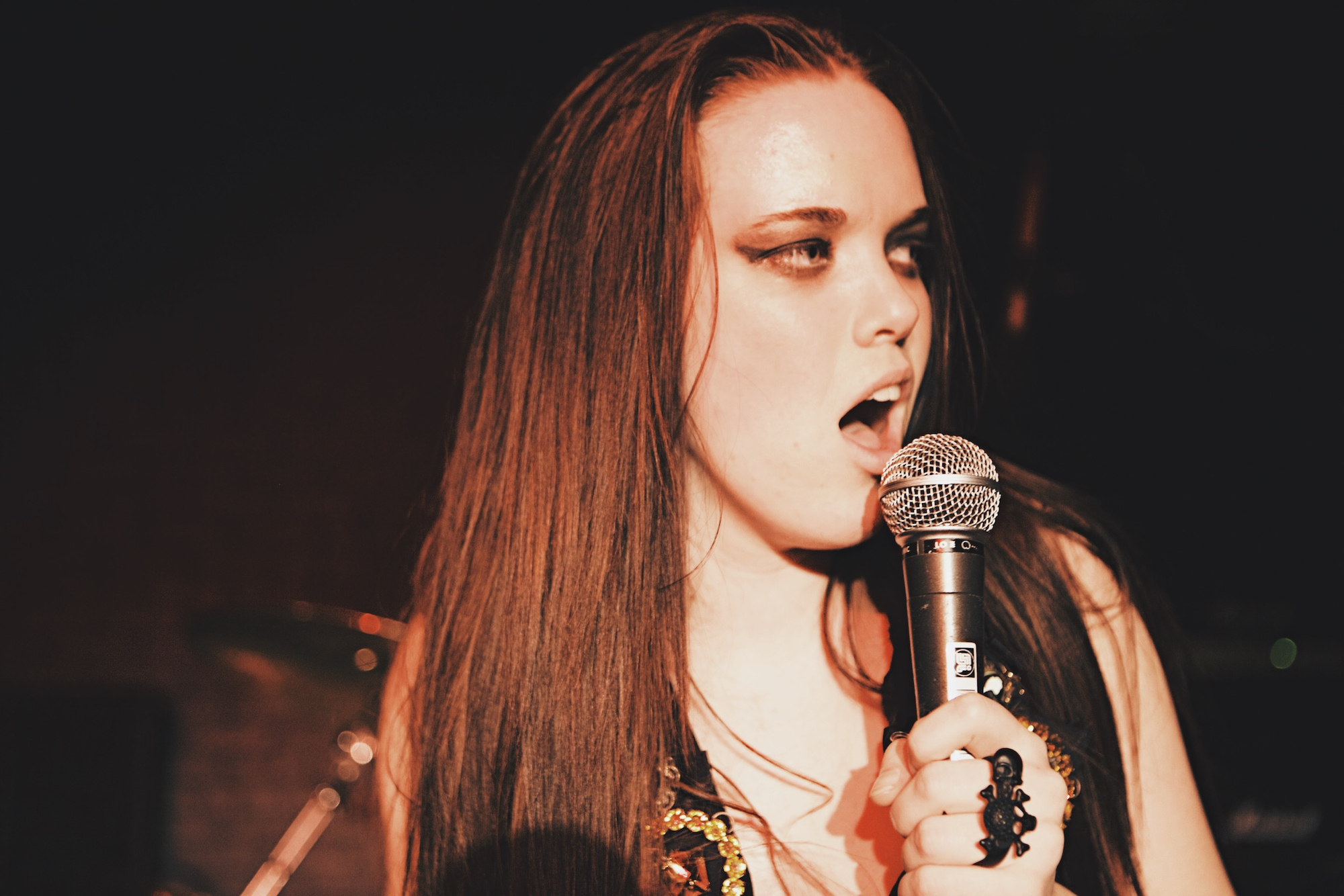 Girl with heavy eye makeup and long hair singing into a microphone.