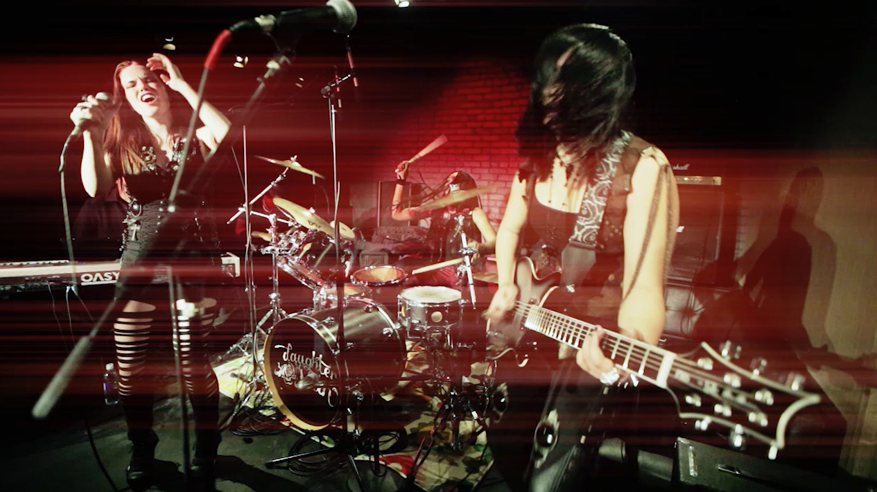 Girls with long hair played guitar and drums onstage performing in red light.