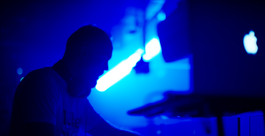 Dj in blue lit nightclub works on providing music