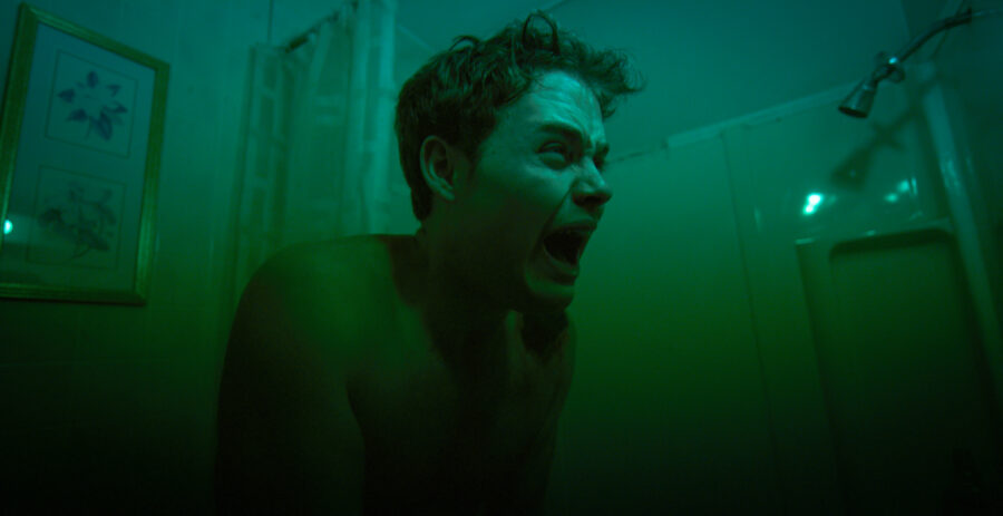 man looks into reflection in a bathroom mirror with dirty green light from the feature film 'FANG' shot by cinematographer Jason Kraynek