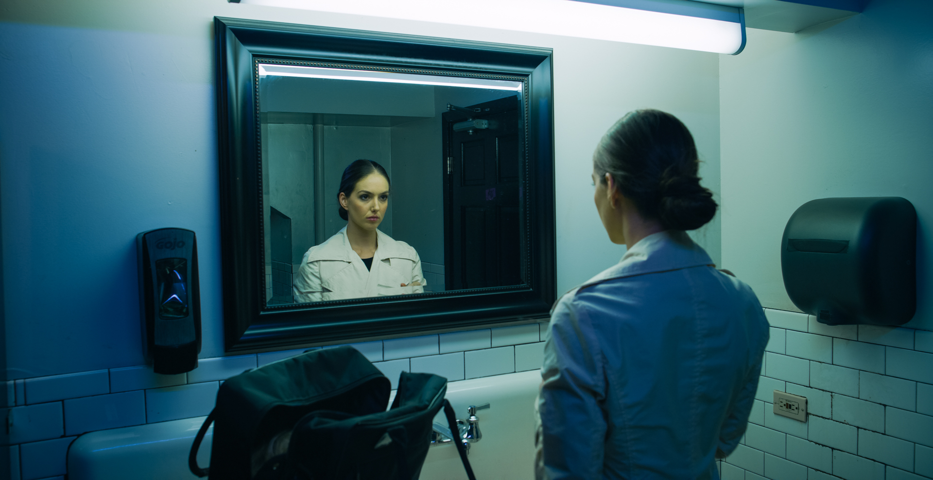 woman in bathroom stares at mirror reflection in the short film 'the Handoff'