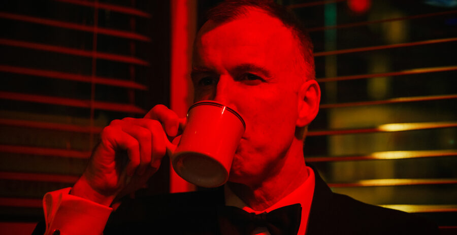 man in red and yellow light drinks coffee in the short film 'the Handoff'