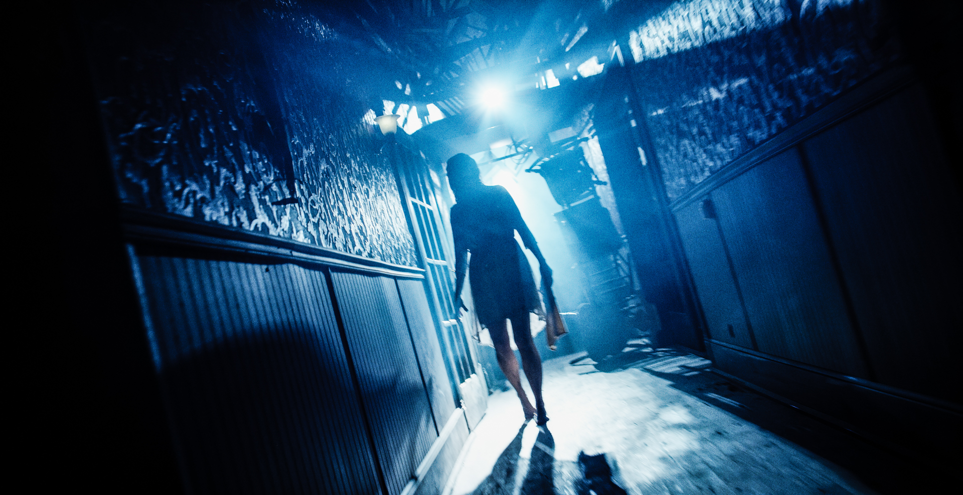 shadowed girl walks out of harshly lit hallway during halloween