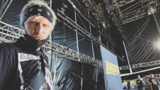 Man onstage with mask in front of lighting truss and Lunachicks banner at Riot Fest.