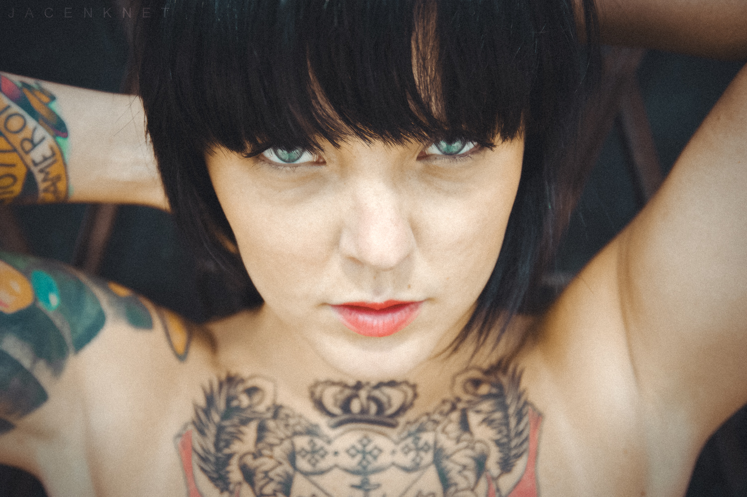 Photo of girl with tattoos and black hair with arms behind head.