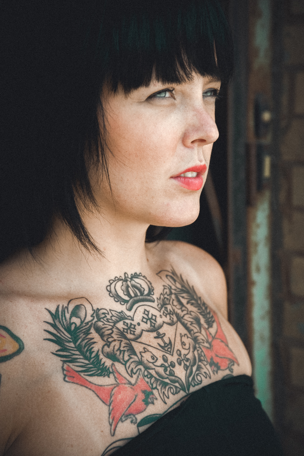 Photo of girl with black hair, tattoos, and black dress looking to the distance.