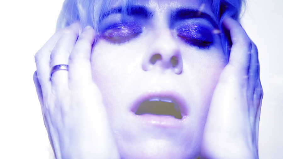 woman mirrored in purple light and blonde hair holds face with mouth open