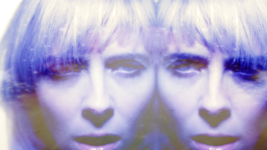 woman mirrored in purple light and blonde hair stares at camera