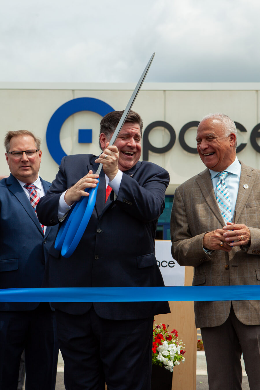 Man holds a pair of large scissors surrounded by men in suits.