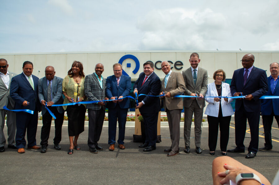 A line of people in suits outside a building cutting a blue ribbon.