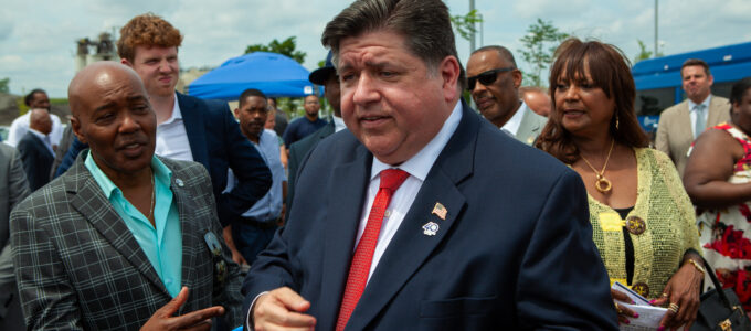 Man in a suit shows off american flag pin surrounded by a crowd of onlookers.