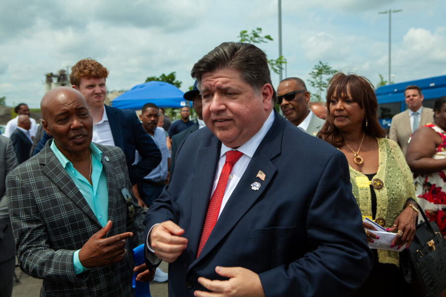 Man in a suit shows off american flag pin surrounded by a crowd of onlookers.