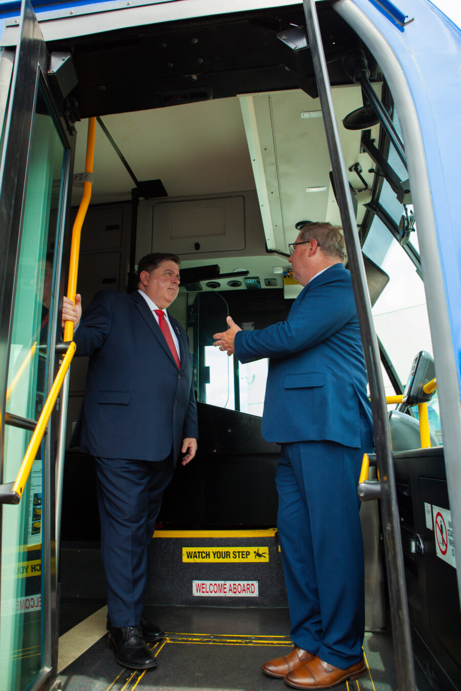 Two men talk inside the steps of a bus.