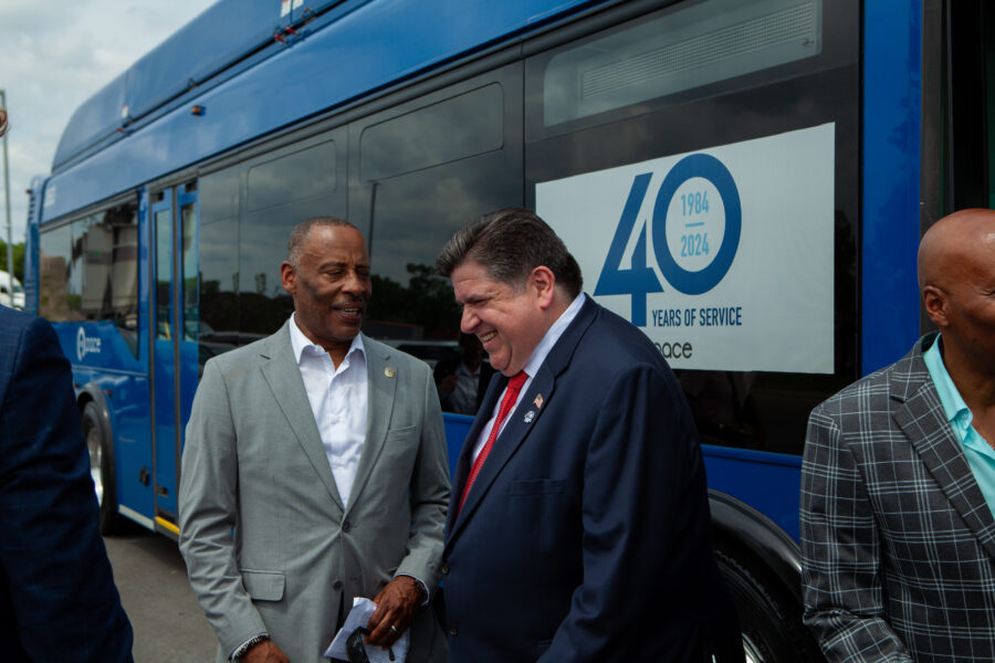 Two men share a laugh standing next to a bus during a sunny day.