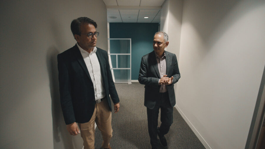 Two men talk with each other in a hallway in suits.