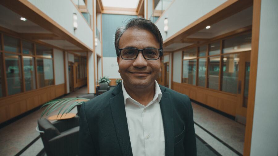 Close shot of a man with glasses smiling in a large open lobby of a building.