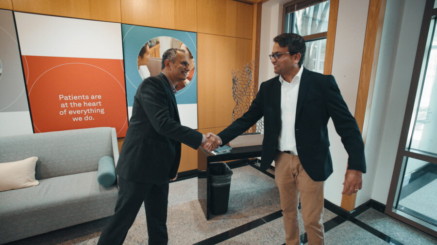 Two men shake hands in a lobby with smiles.