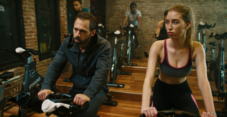 Actor in a advertisment campaign short film for Steel Supplements trains on bikes at a gym