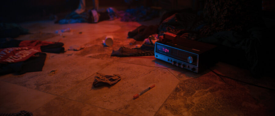 Drug items and clothes spread out in a dark bathroom floor.