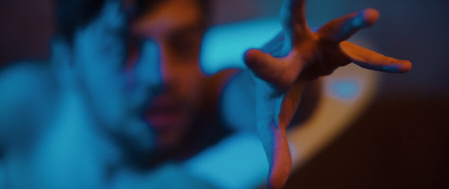 Man reaches out towards the screen while in a bathtub lit with blue and orange lights.