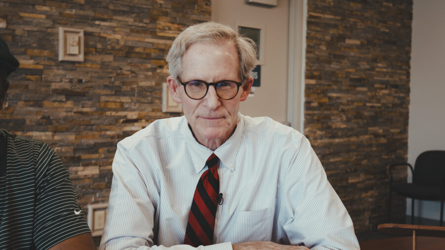 A man with glasses looking into a camera inside a conference room.