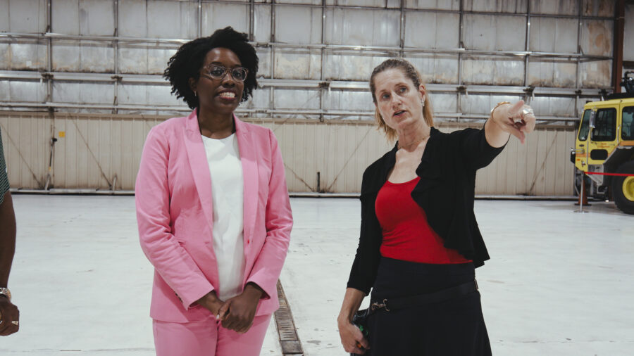 Two woman in conversation inside a airplane hanger.