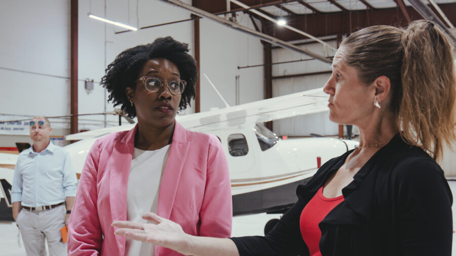 Two woman in conversation inside a airplane hanger.