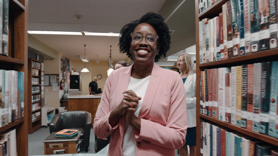 Woman in pink suit walks towards camera.