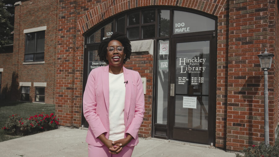 Woman in pink suit talks to camera.