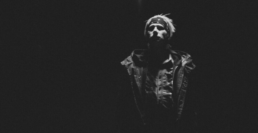 Man in shadows looks up with coat and bandana.